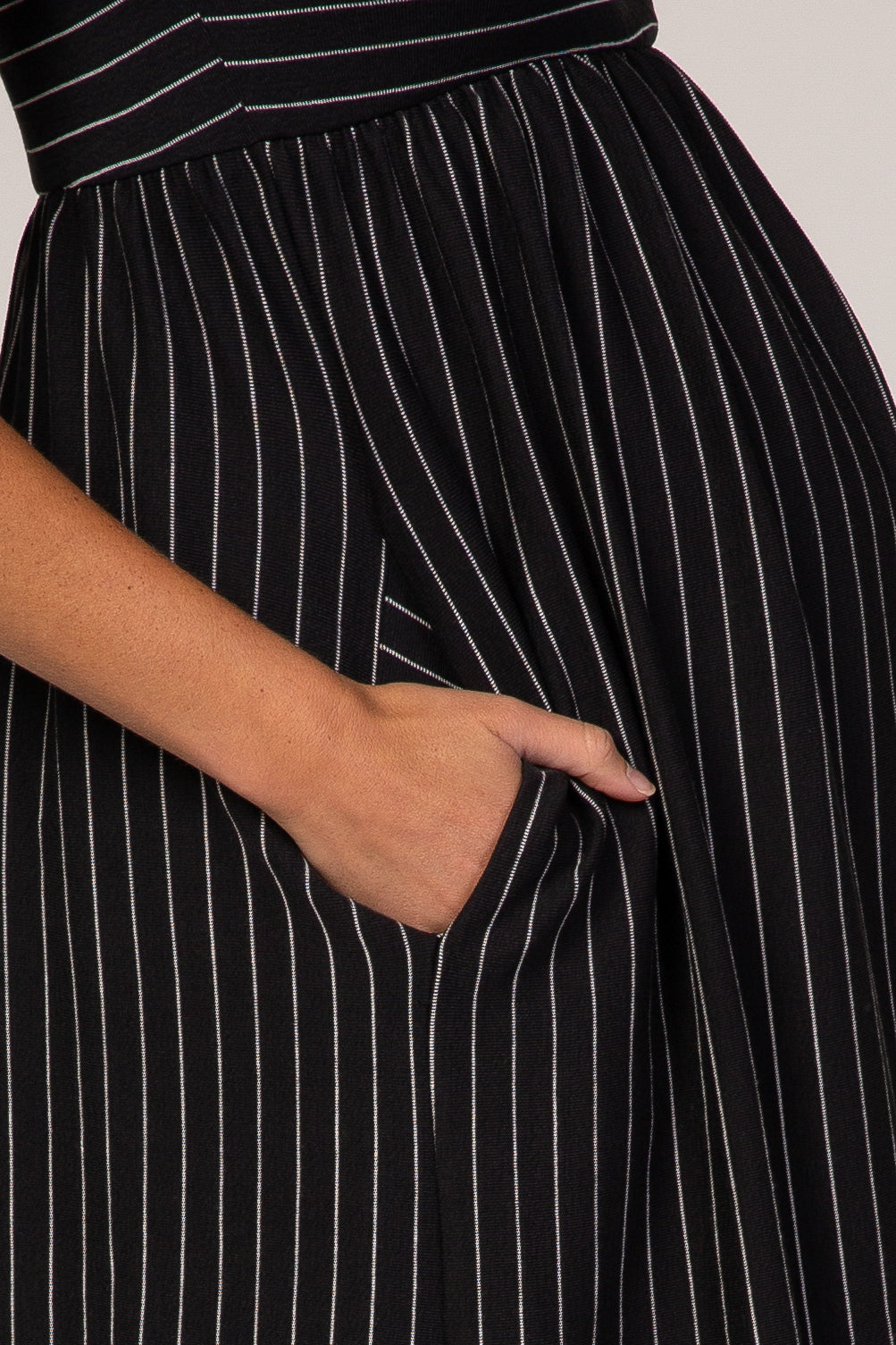 close-up of a hand in the pocket of a black and white striped maternity dress with an empire waist