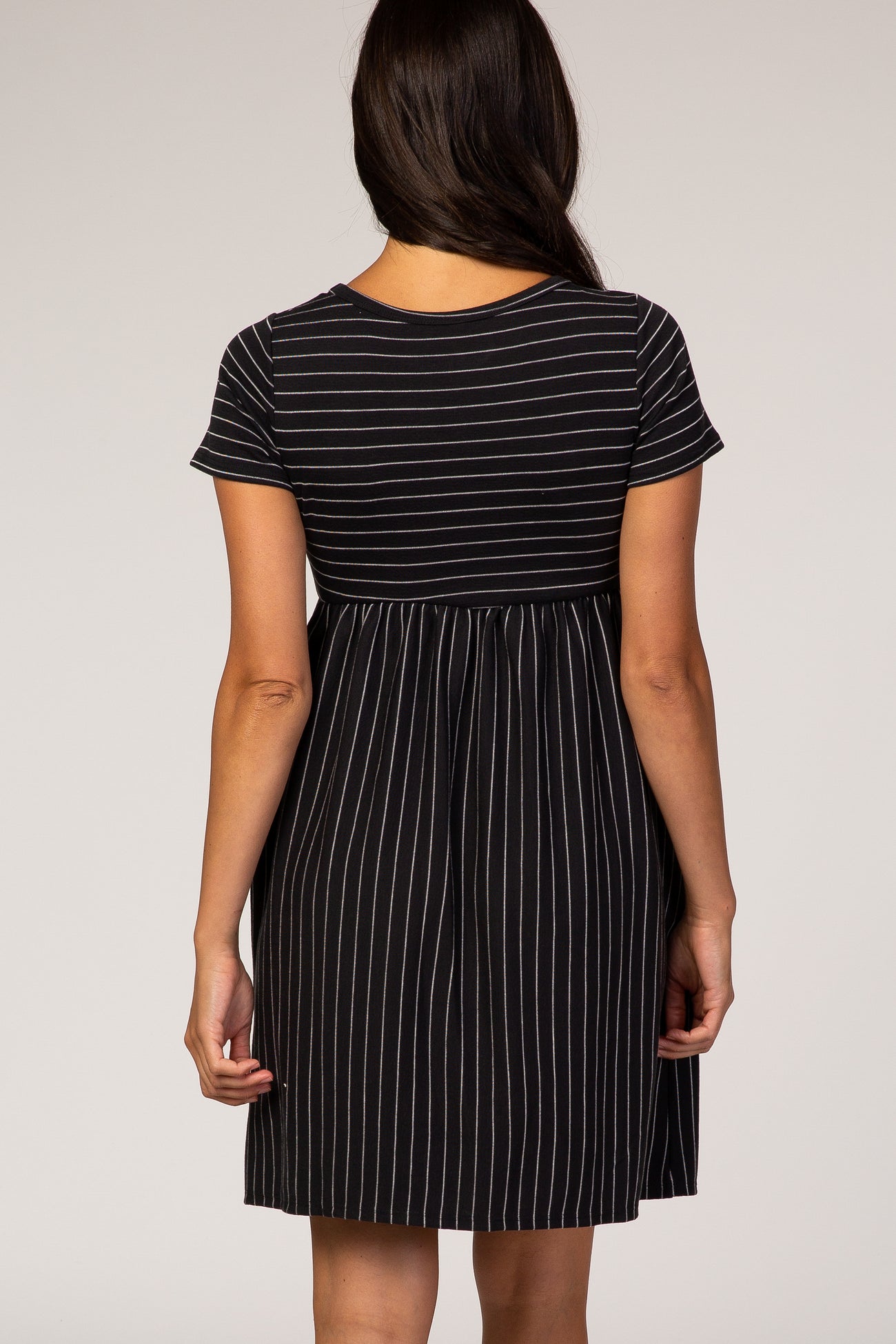 woman wearing a black and white striped short sleeve dress with a gathered waist and a flared skirt from the back