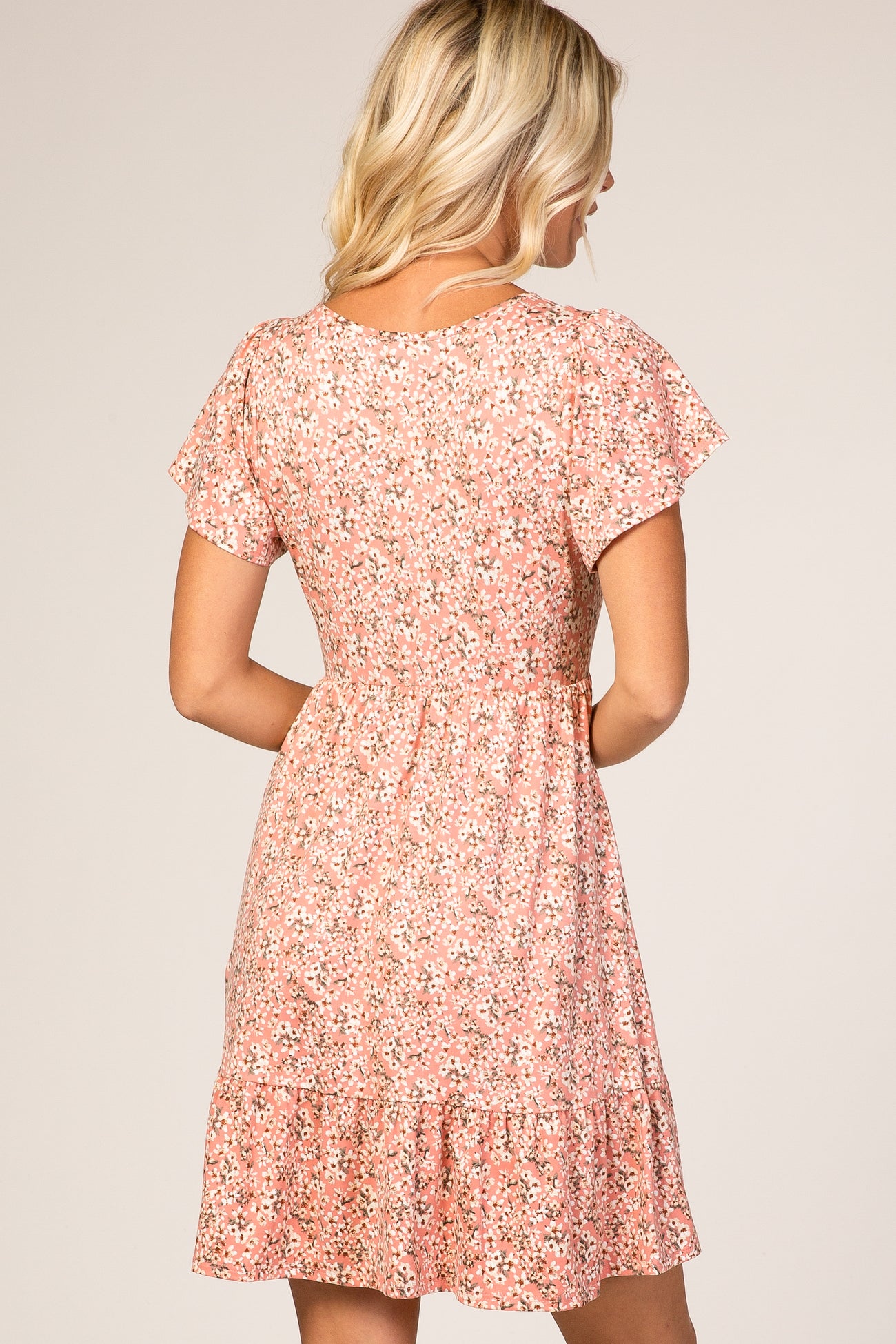 woman wearing a pink floral short-sleeve dress with a tiered ruffle hem and a fitted waist, viewed from the back