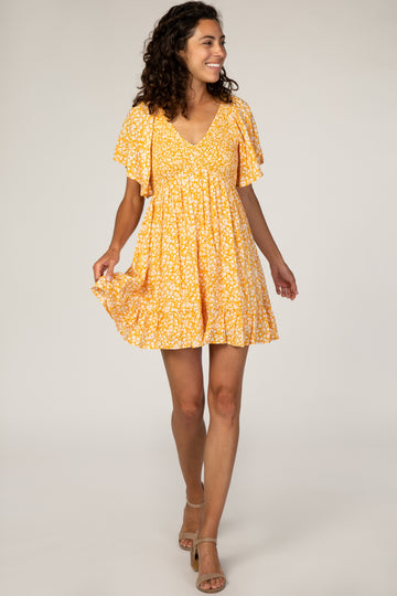 woman wearing a yellow short sleeve floral dress with a v-neck and flared skirt, smiling and walking