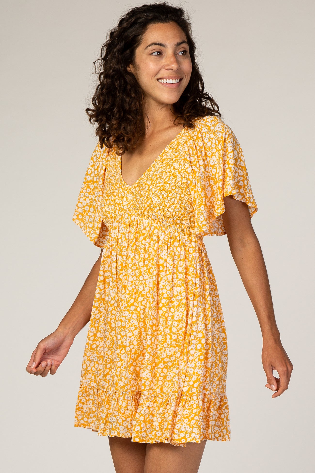 woman wearing a yellow floral short dress with a v-neckline and flutter sleeves