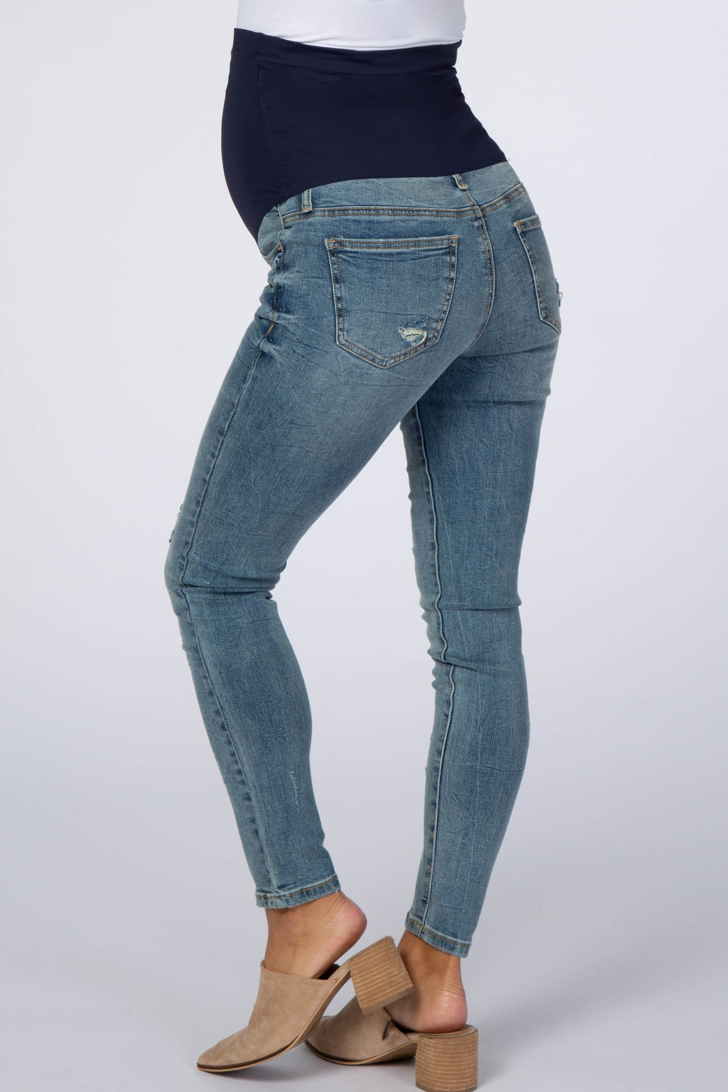 woman wearing blue distressed maternity skinny jeans with navy belly band and tan block heel mules