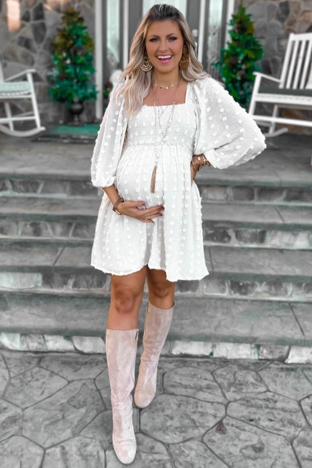 woman wearing a white maternity dress with puff sleeves and a baby bump, standing on steps with knee-high boots