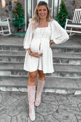 woman wearing a white maternity dress with puff sleeves and a baby bump, standing on steps with knee-high boots