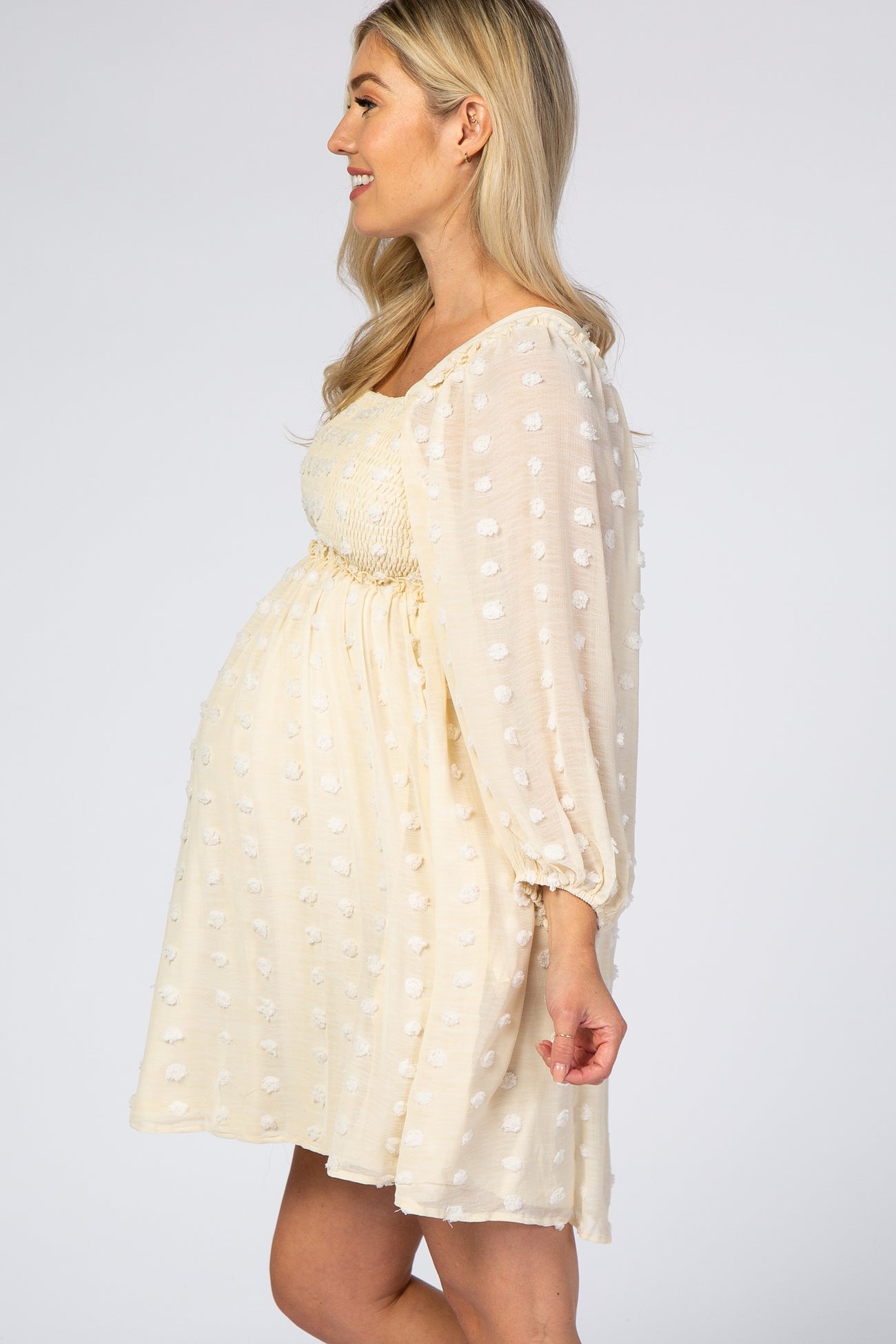 woman wearing a light yellow maternity dress with textured polka dots and puff sleeves, showing her baby bump