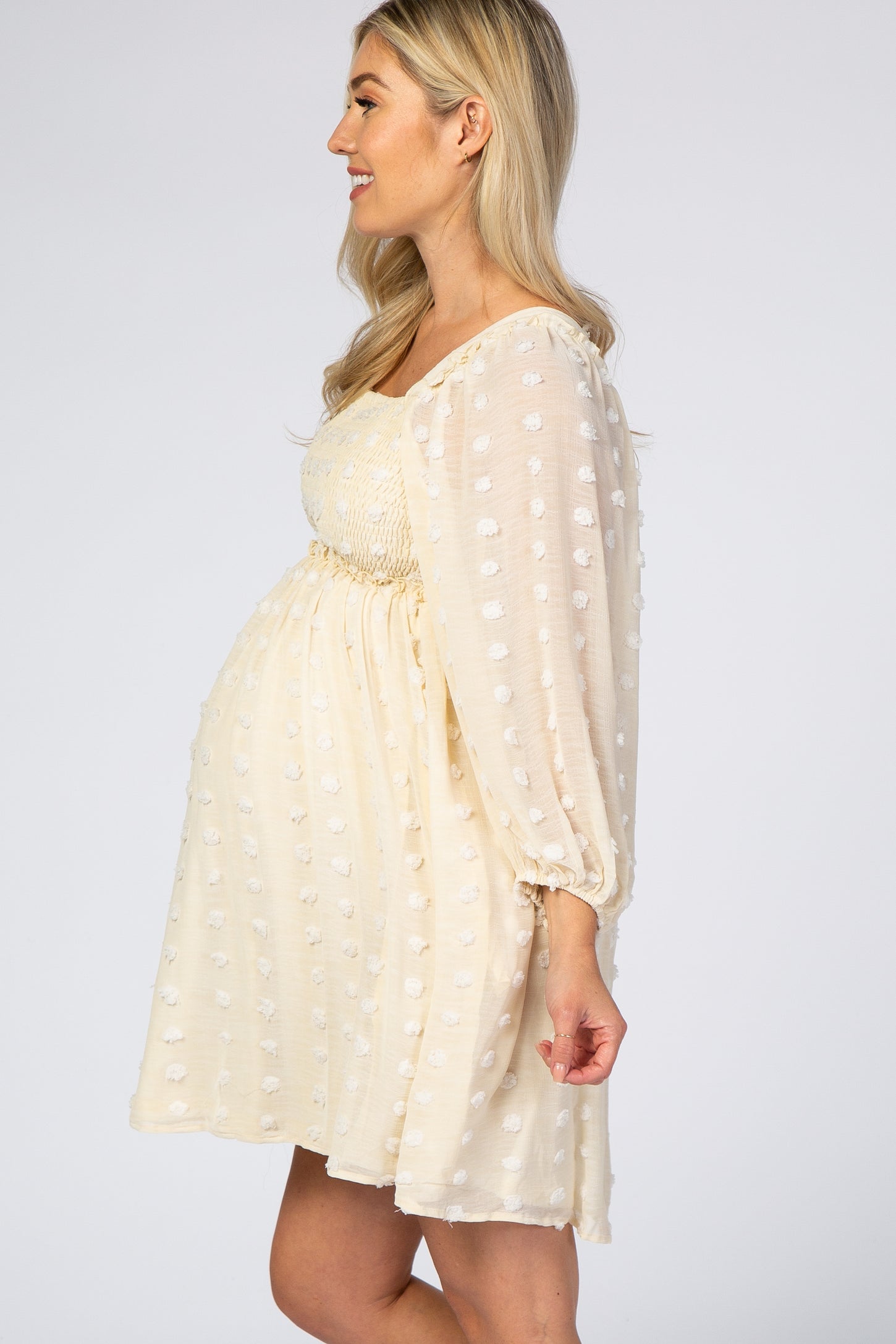 woman wearing a light yellow maternity dress with textured polka dots and puff sleeves, showing her baby bump