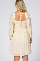 Back view of a woman wearing a cream swiss dot maternity dress with long puff sleeves and a smocked back.