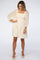woman wearing a cream-colored dress with puff sleeves and a smocked bodice, standing and smiling