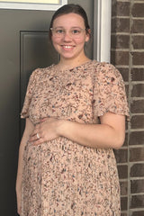 woman wearing a floral print maternity dress with short puff sleeves and holding her baby bump