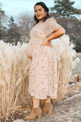 pregnant woman in floral midi dress and tan ankle boots posing in front of tall pampas grass