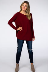 woman wearing a burgundy long sleeve top with a relaxed fit, paired with distressed dark jeans and ankle boots
