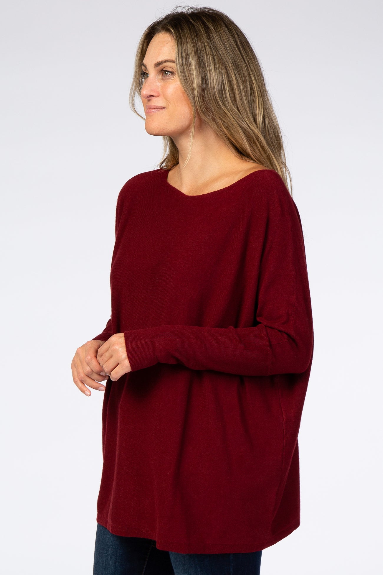 woman wearing a burgundy oversized knit sweater and blue jeans against a white background