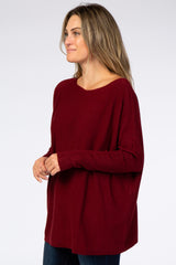 woman wearing a burgundy oversized knit sweater and blue jeans against a white background