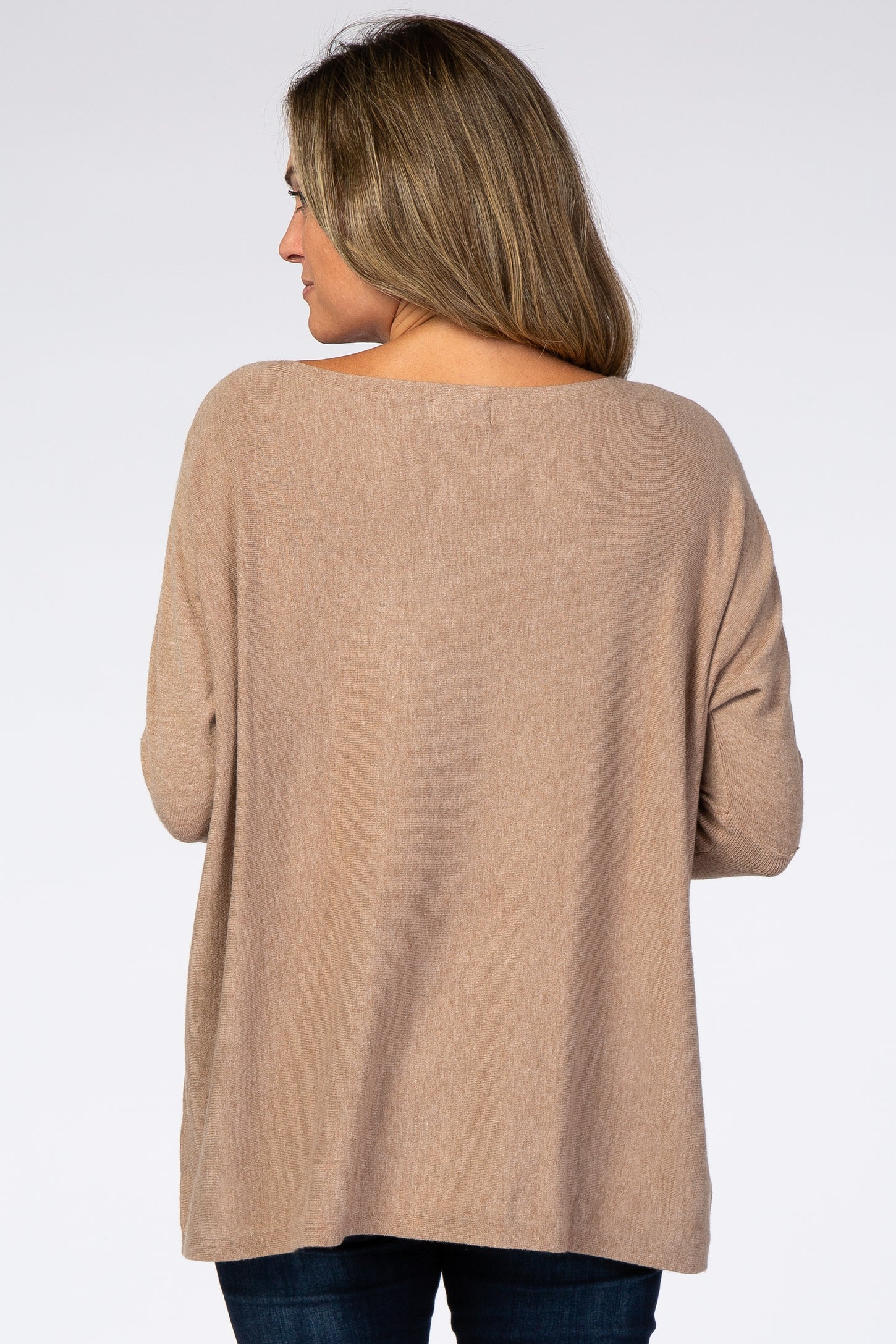 Back view of a woman wearing a tan long sleeve boat neck maternity sweater with dark blue jeans