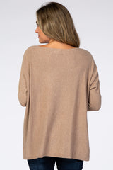Back view of a woman wearing a tan long sleeve boat neck maternity sweater with dark blue jeans