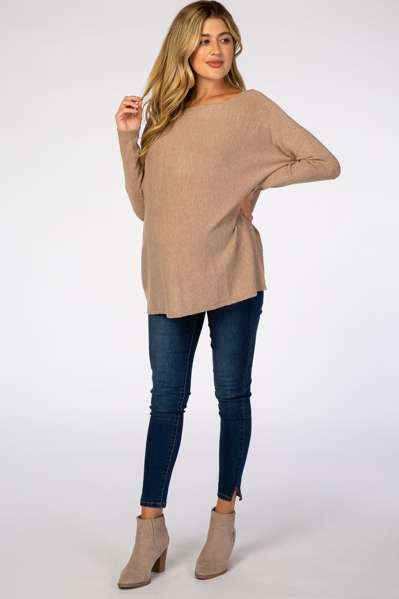 woman wearing a beige maternity sweater with a loose fit and a visible baby bump, paired with dark skinny jeans and ankle boots