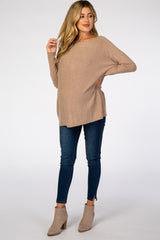 woman wearing a beige maternity sweater with a loose fit and a visible baby bump, paired with dark skinny jeans and ankle boots