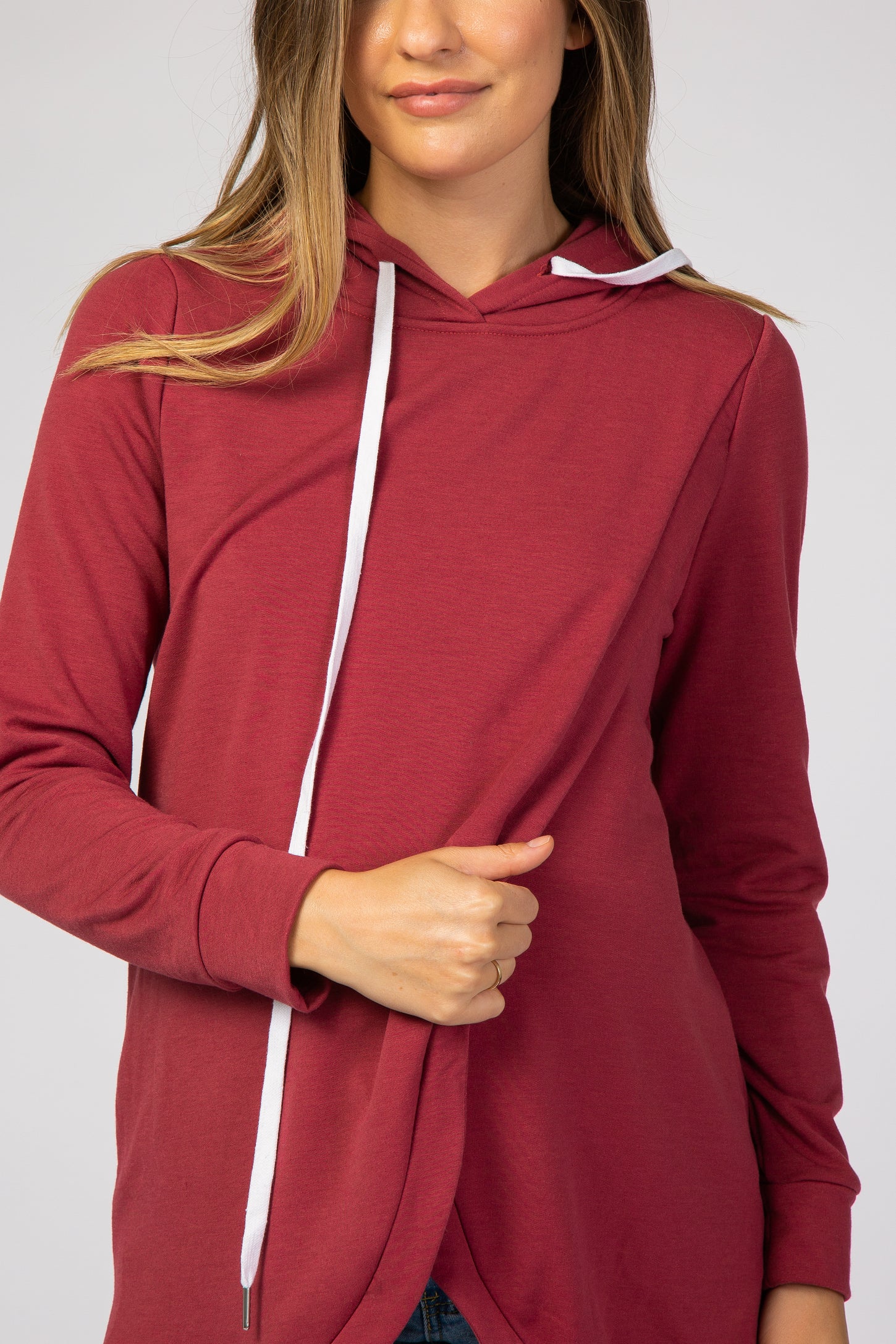woman wearing a burgundy maternity hoodie with a white drawstring and long sleeves, gently holding her baby bump