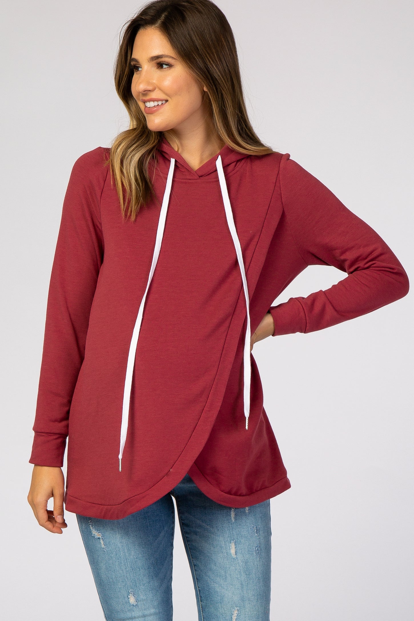 woman wearing a burgundy maternity hoodie with a crossover design and white drawstrings, styled with jeans