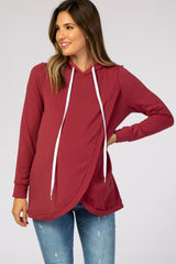 woman wearing a burgundy maternity hoodie with a crossover design and white drawstrings, styled with jeans