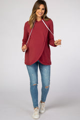 woman wearing a burgundy maternity hoodie with a crossover design and drawstring, paired with distressed skinny jeans