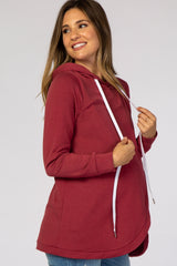 woman wearing a burgundy maternity hoodie with a scalloped hem and a white drawstring, showcasing her baby bump