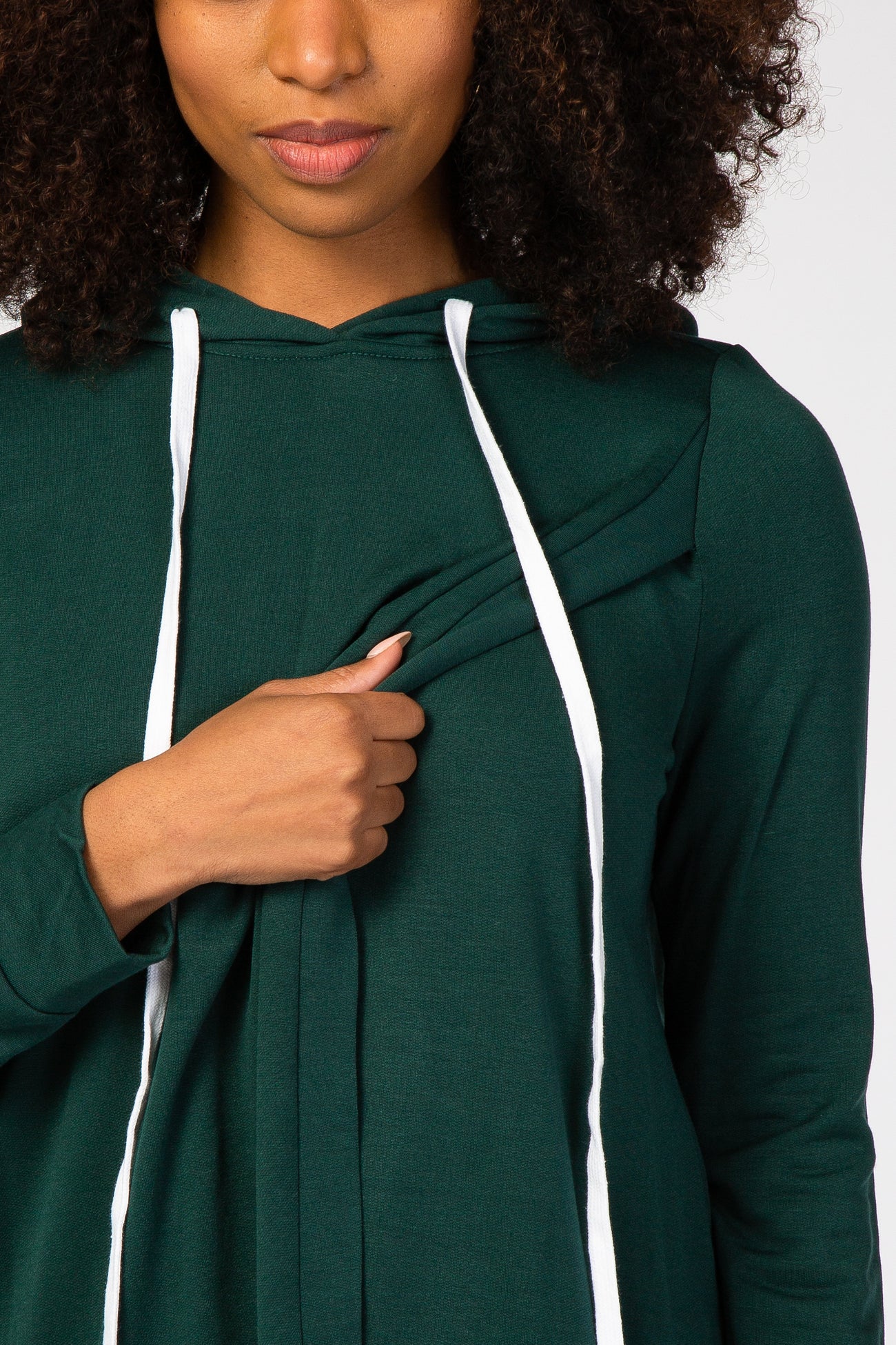 Woman wearing a dark green nursing hoodie with white drawstrings and a lift-up flap for breastfeeding access.