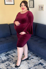 woman wearing a burgundy maternity dress with bell sleeves, showing her baby bump while standing on a couch