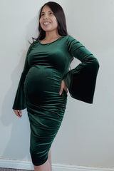 woman wearing a dark green velvet maternity dress with bell sleeves and a visible baby bump