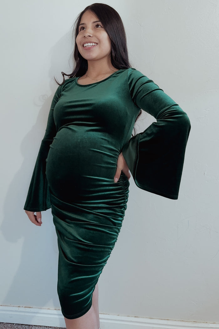 woman wearing a dark green velvet maternity dress with bell sleeves and a visible baby bump