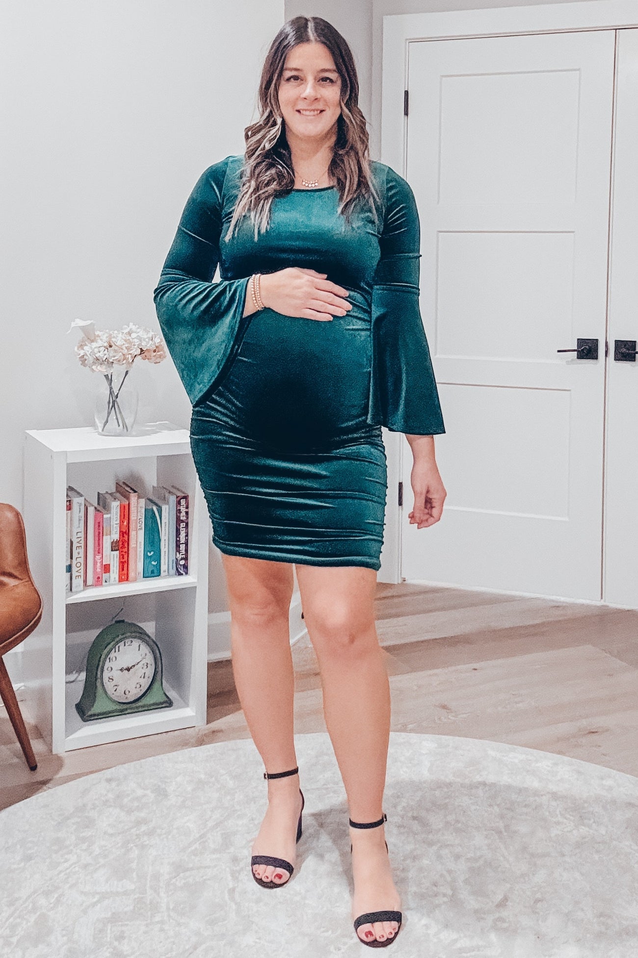 woman wearing a green velvet maternity dress with bell sleeves and a visible baby bump