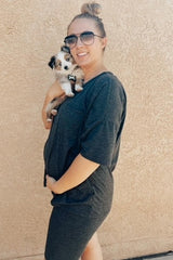 smiling pregnant woman in charcoal grey maternity dress holding a small australian shepherd puppy