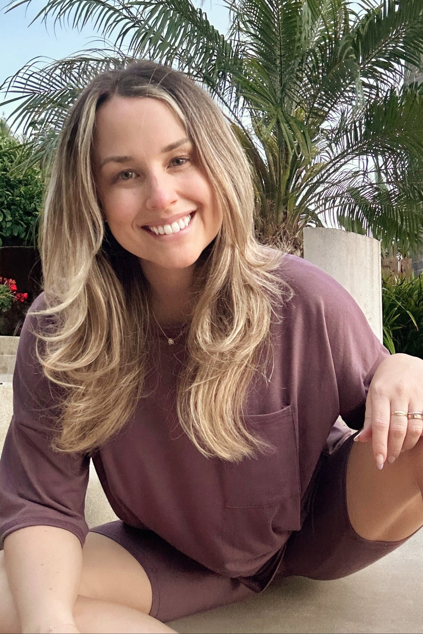 woman wearing a mauve oversized short sleeve lounge set with a pocket, smiling while sitting outdoors