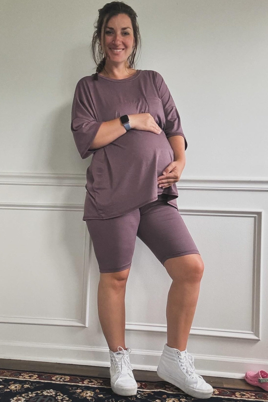 woman wearing a mauve maternity top and matching bike shorts, showing her baby bump while smiling