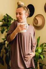 woman wearing a dusty rose oversized maternity top and holding a mug while gently cradling her baby bump
