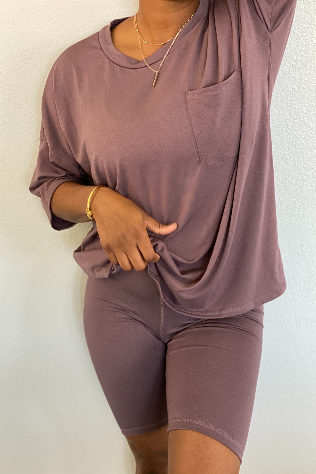 woman wearing a mauve oversized t-shirt with a pocket and matching bike shorts, styling with layered necklaces