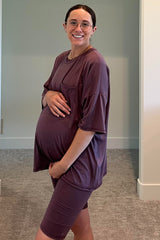woman wearing a mauve oversized maternity t-shirt and matching bike shorts, gently cradling her baby bump