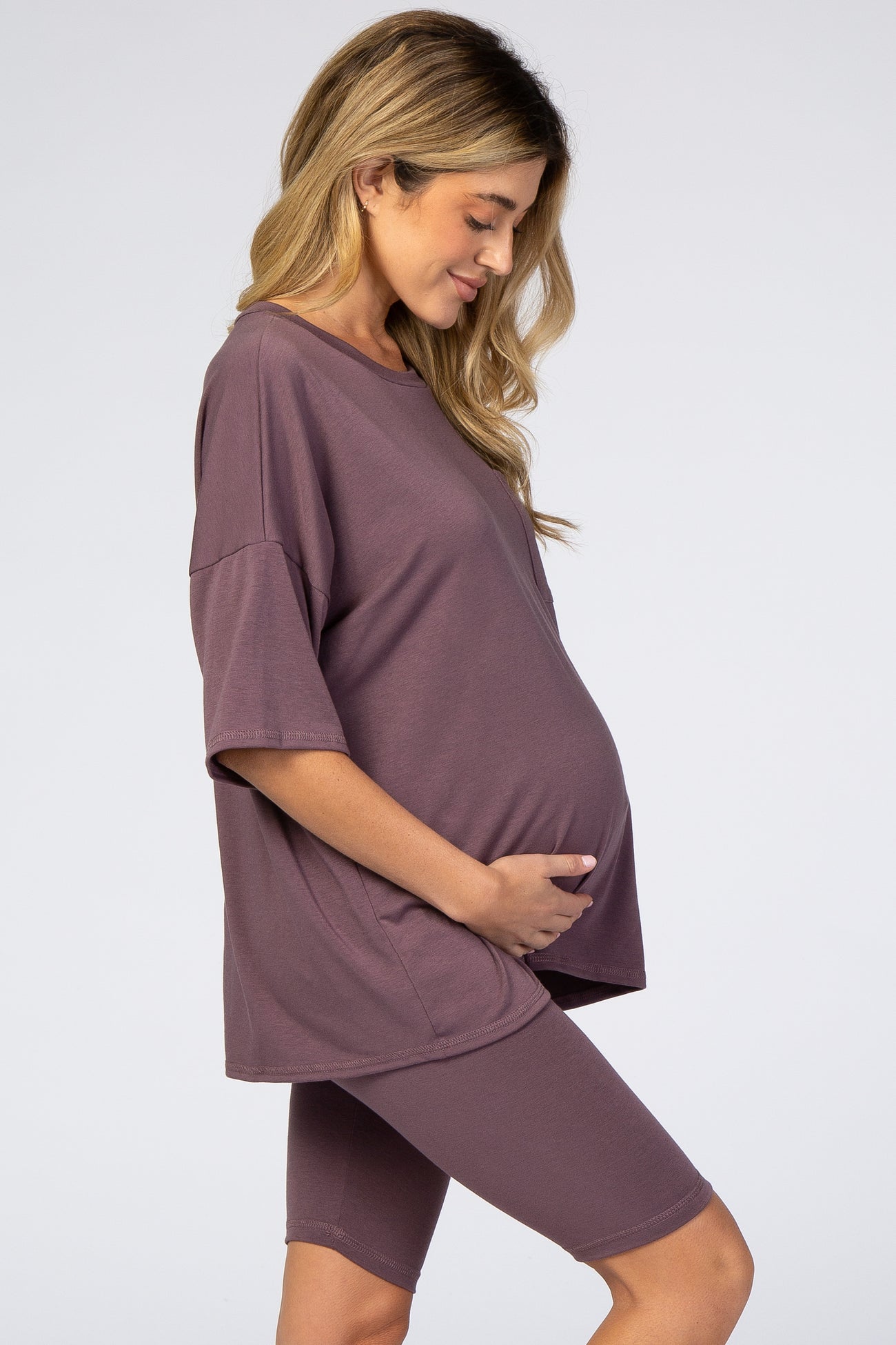 woman wearing a mauve oversized maternity tee and matching bike shorts, cradling her baby bump