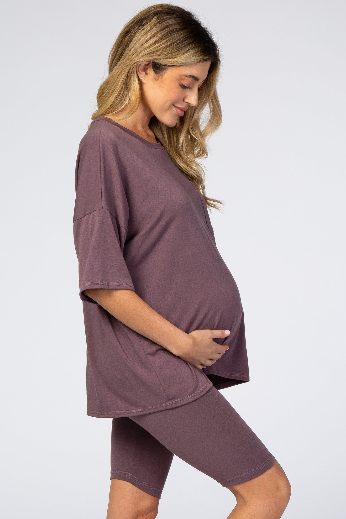 woman wearing a mauve oversized maternity tee and matching bike shorts, cradling her baby bump