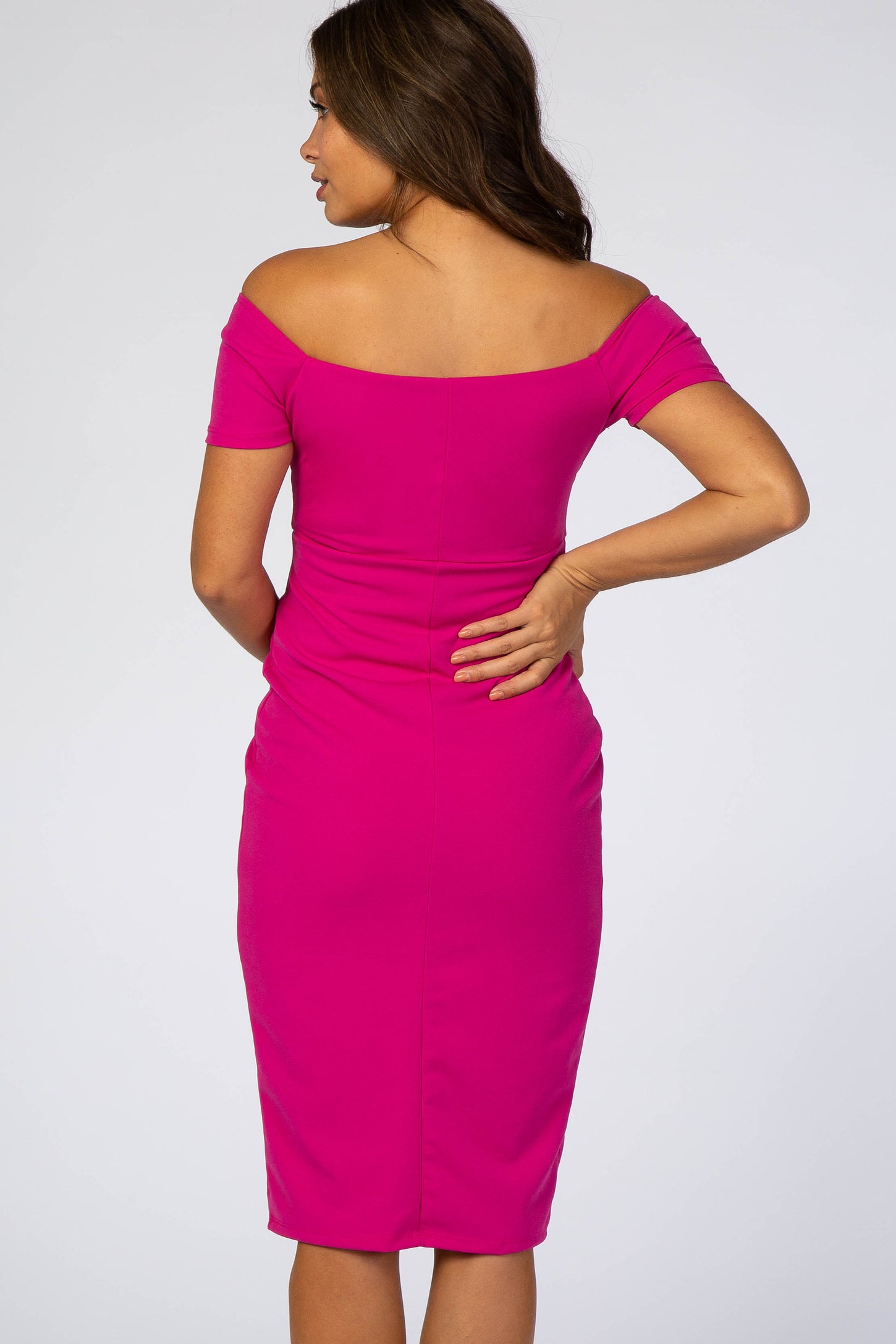 woman wearing a bright pink off-shoulder maternity dress, showing a fitted silhouette from the back