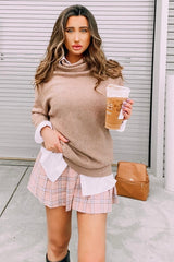 woman wearing a beige sweater layered over a white shirt with a pink plaid skirt, holding an iced coffee drink