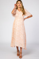 woman wearing a light peach floral maternity dress with short sleeves and a smocked bodice, standing with one hand on her hair