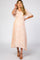 woman wearing a light peach floral maternity dress with short sleeves and a smocked bodice, standing with one hand on her hair