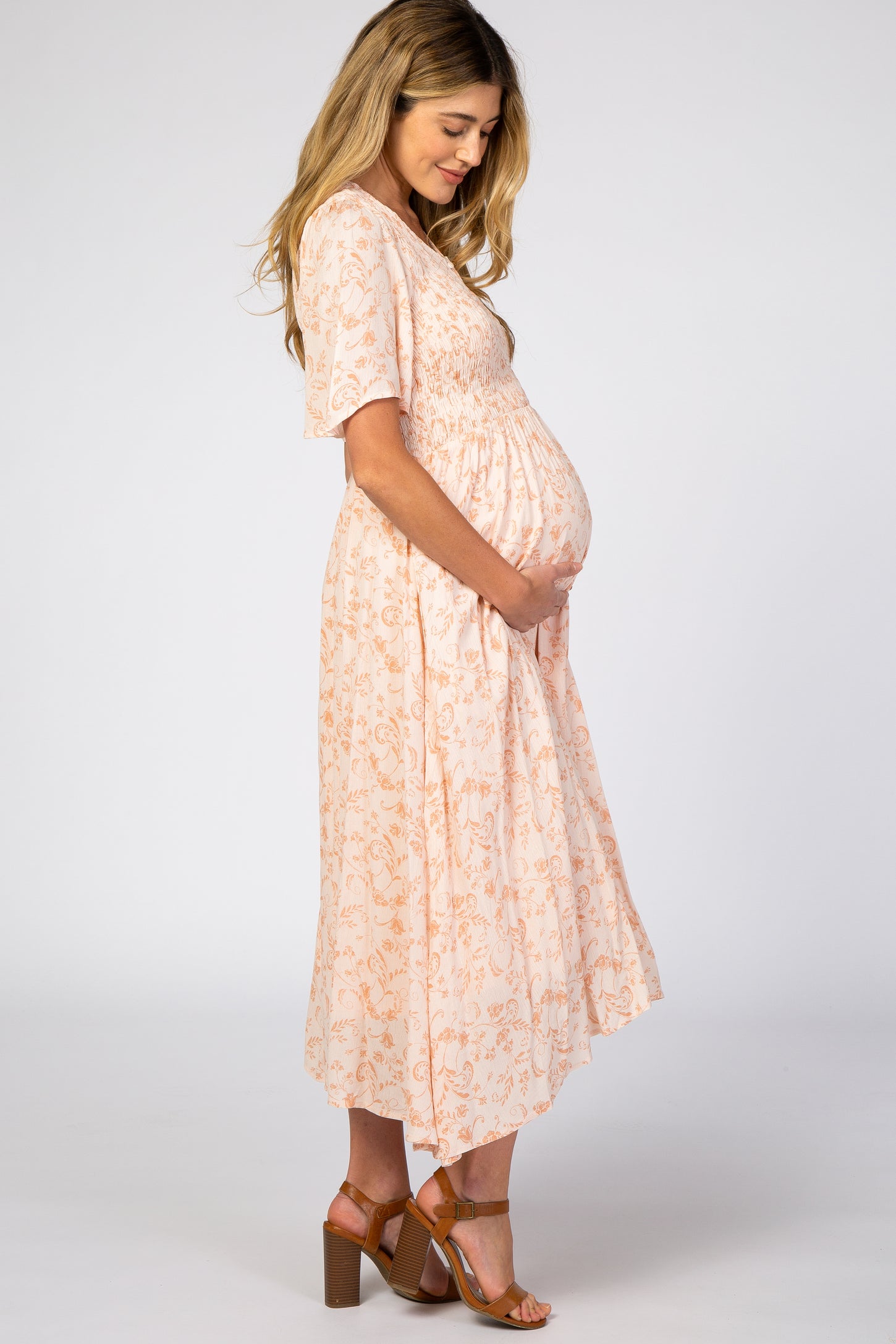 woman wearing a peach floral maternity dress with short sleeves and a baby bump, standing sideways
