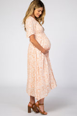 woman wearing a peach floral maternity dress with short sleeves and a baby bump, standing sideways