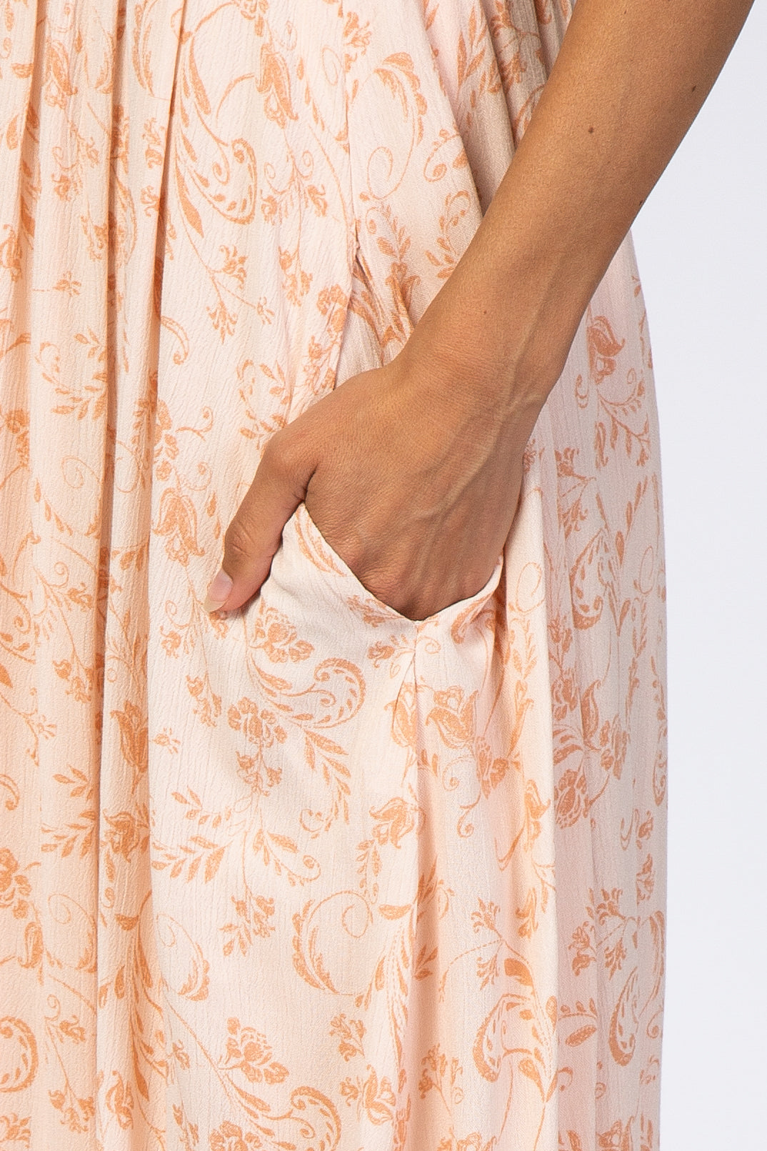 close-up of a woman’s hand in the pocket of a light peach floral print maxi dress with textured fabric