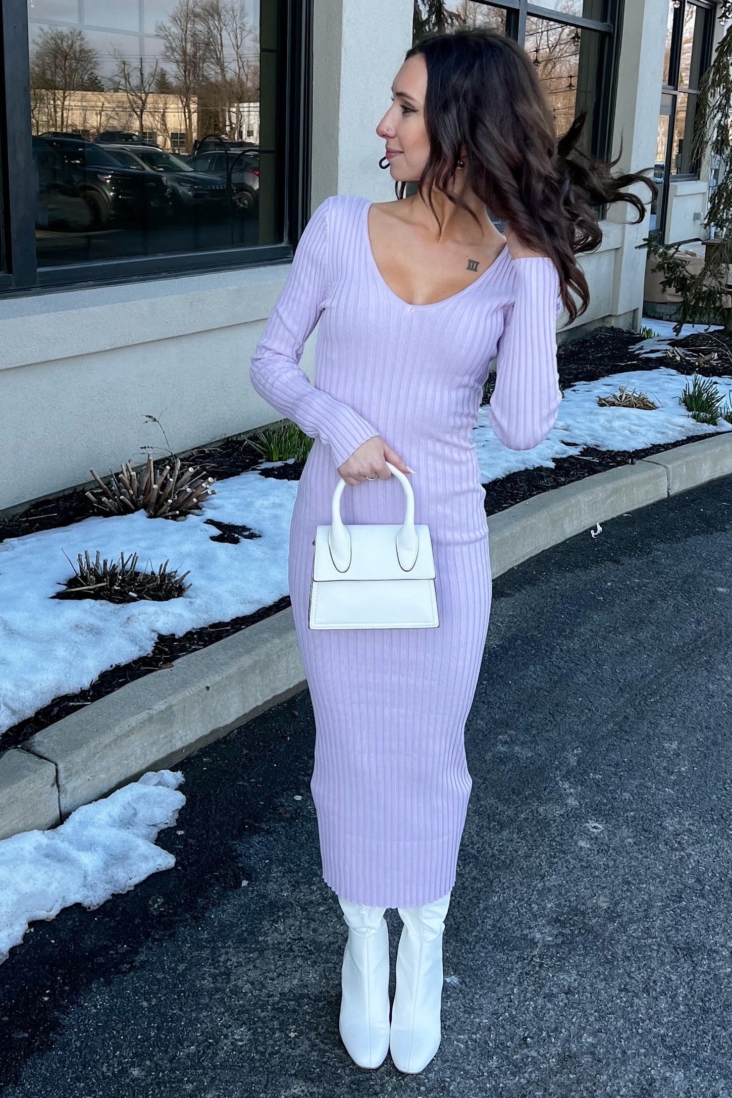 woman wearing a lilac ribbed long sleeve dress paired with white knee-high boots and holding a small white handbag