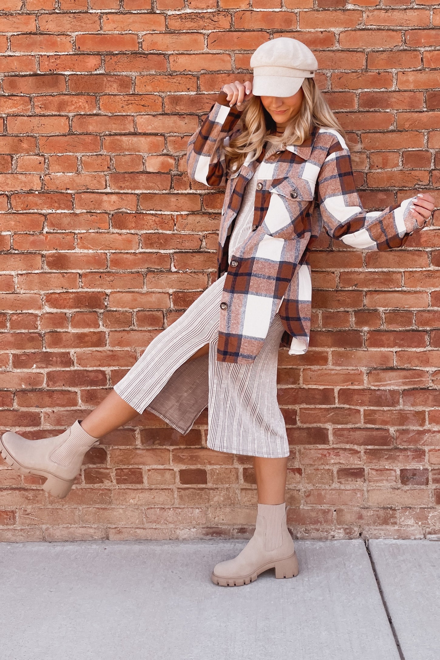 woman in plaid shacket, ribbed midi dress, and beige chelsea boots posing against a brick wall