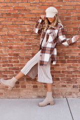 woman in plaid shacket, ribbed midi dress, and beige chelsea boots posing against a brick wall