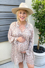 woman wearing a floral long sleeve maternity dress and holding her baby bump, accessorized with a wide-brimmed hat